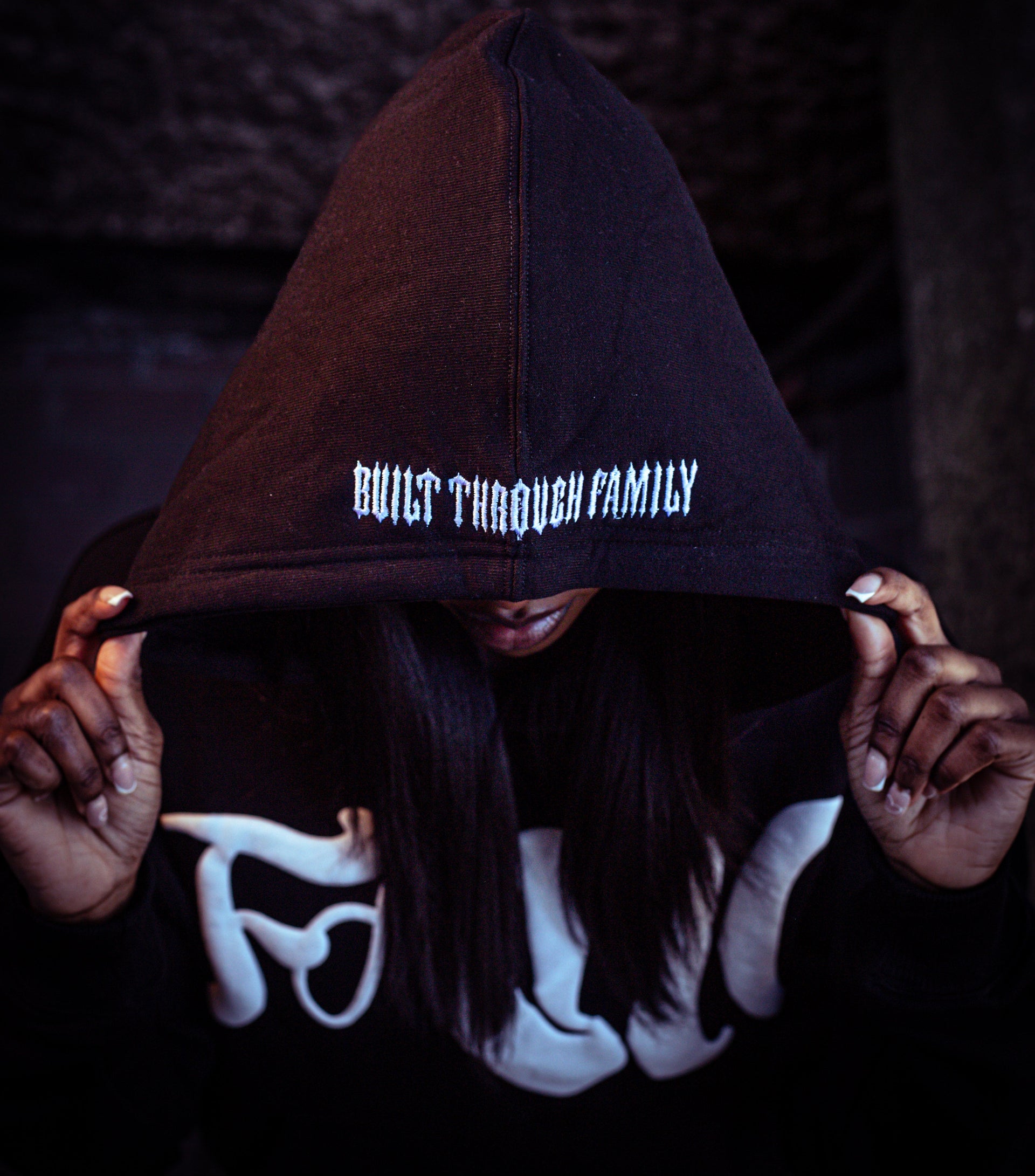 Person wearing a hoodie with 'Built Through Family' text in a dark setting
